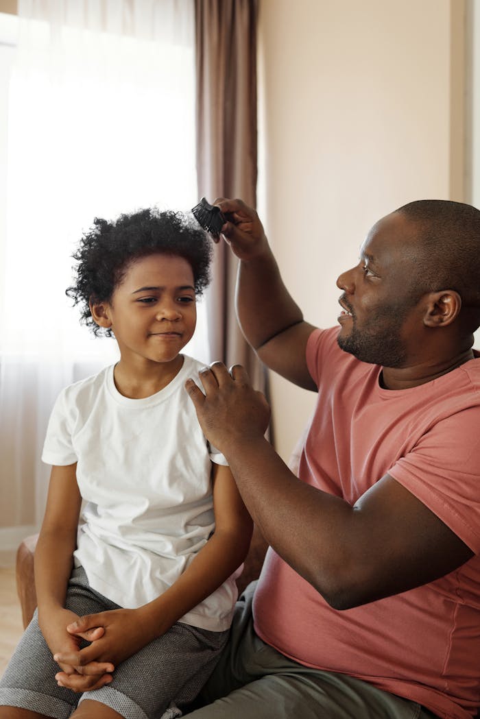A father brushes his sons curly hair, showcasing love and parenthood indoors.
